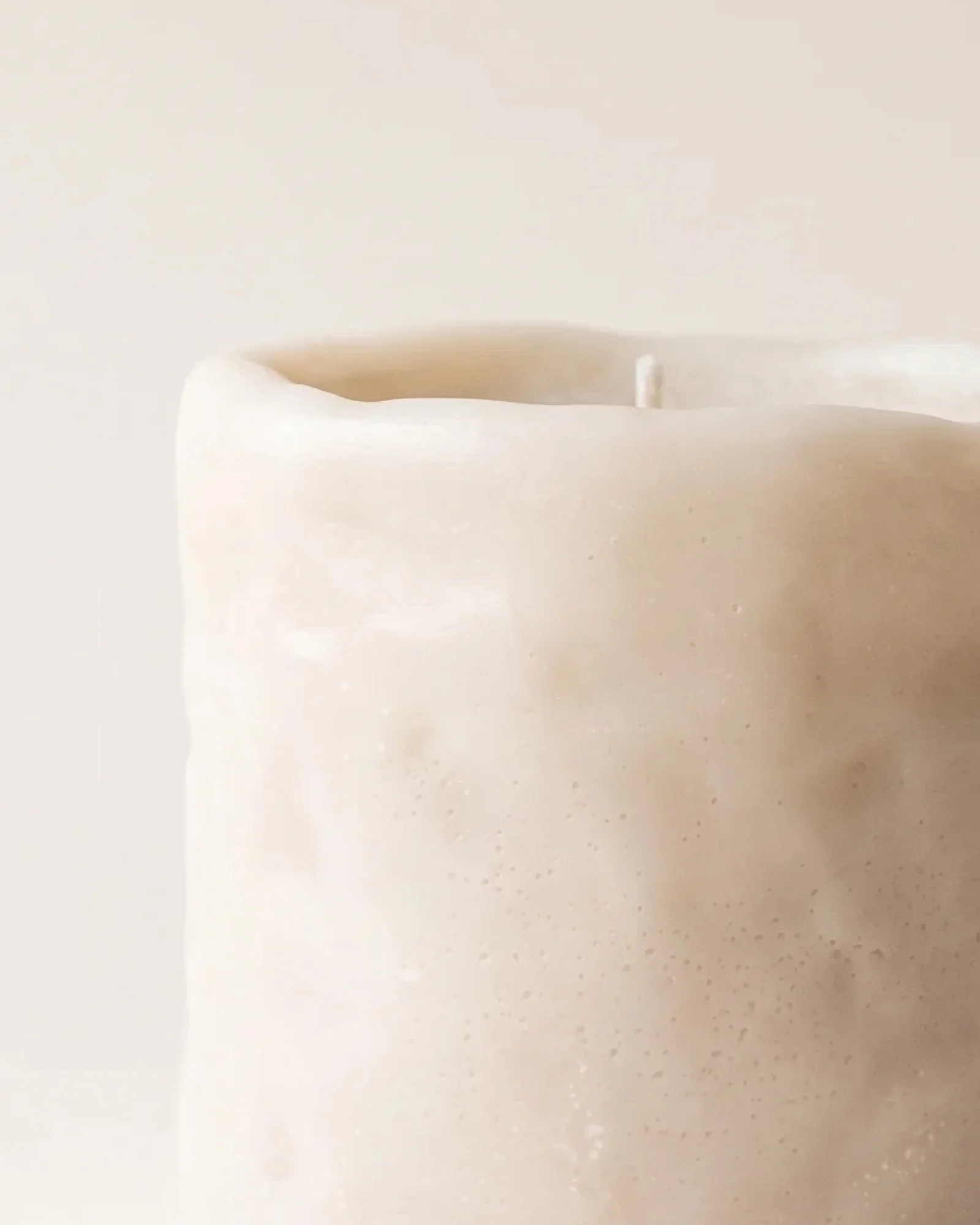 Lit light-coloured Clay Cylinder decorative candle with melted wax around the wick