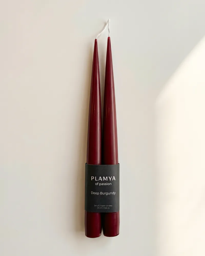 Sculptural burgundy candles with a smooth, columnar form standing upright against a neutral background.