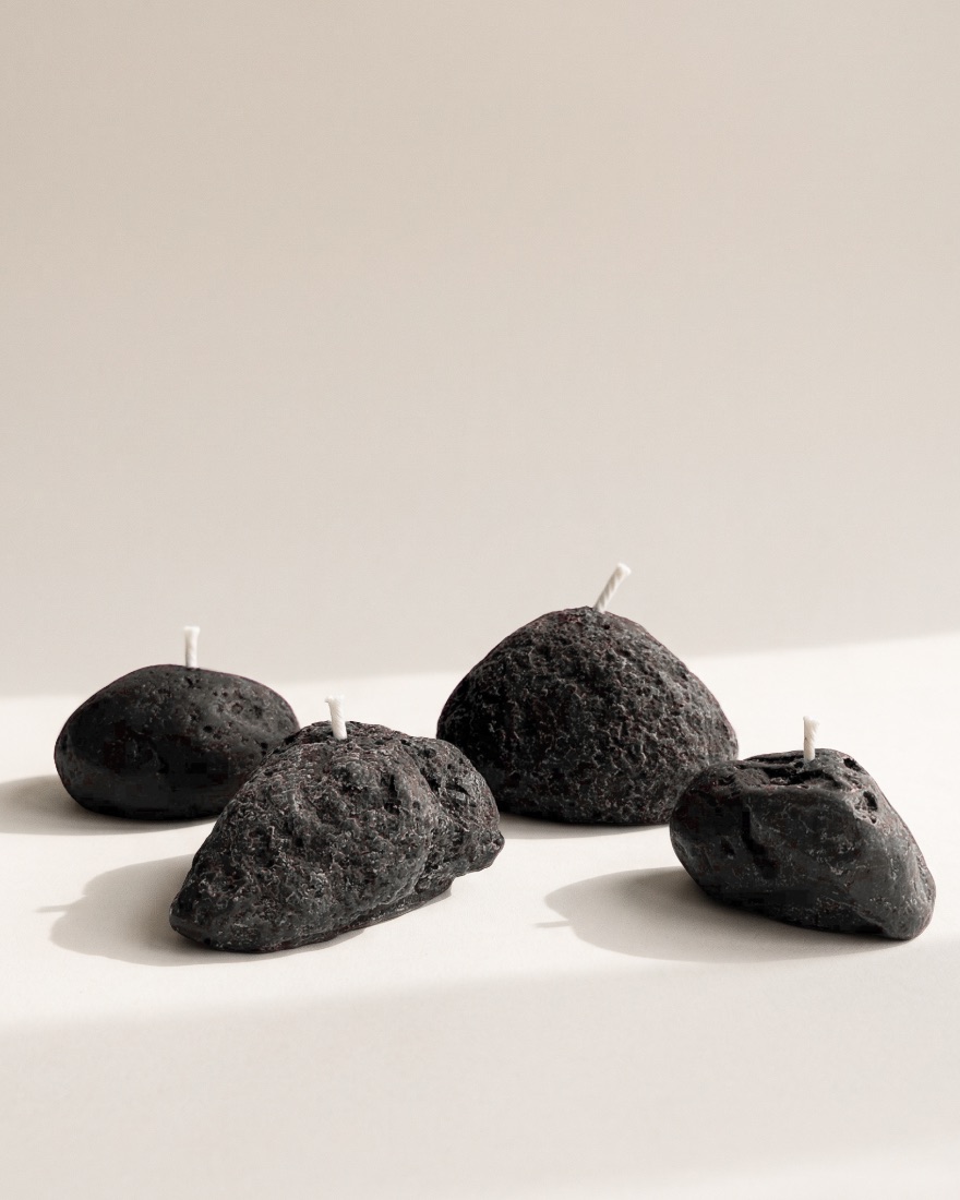 Four black Volcanic Stone candles with pitted, lava-like surfaces on a pale stone backdrop.