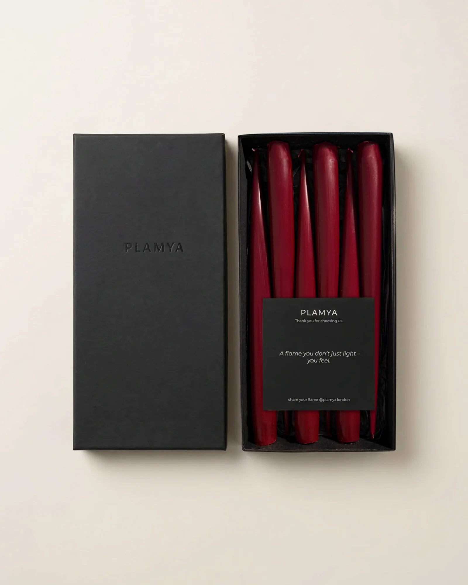 Open black PLAMYA box containing six Vivid Red taper candles and a message card