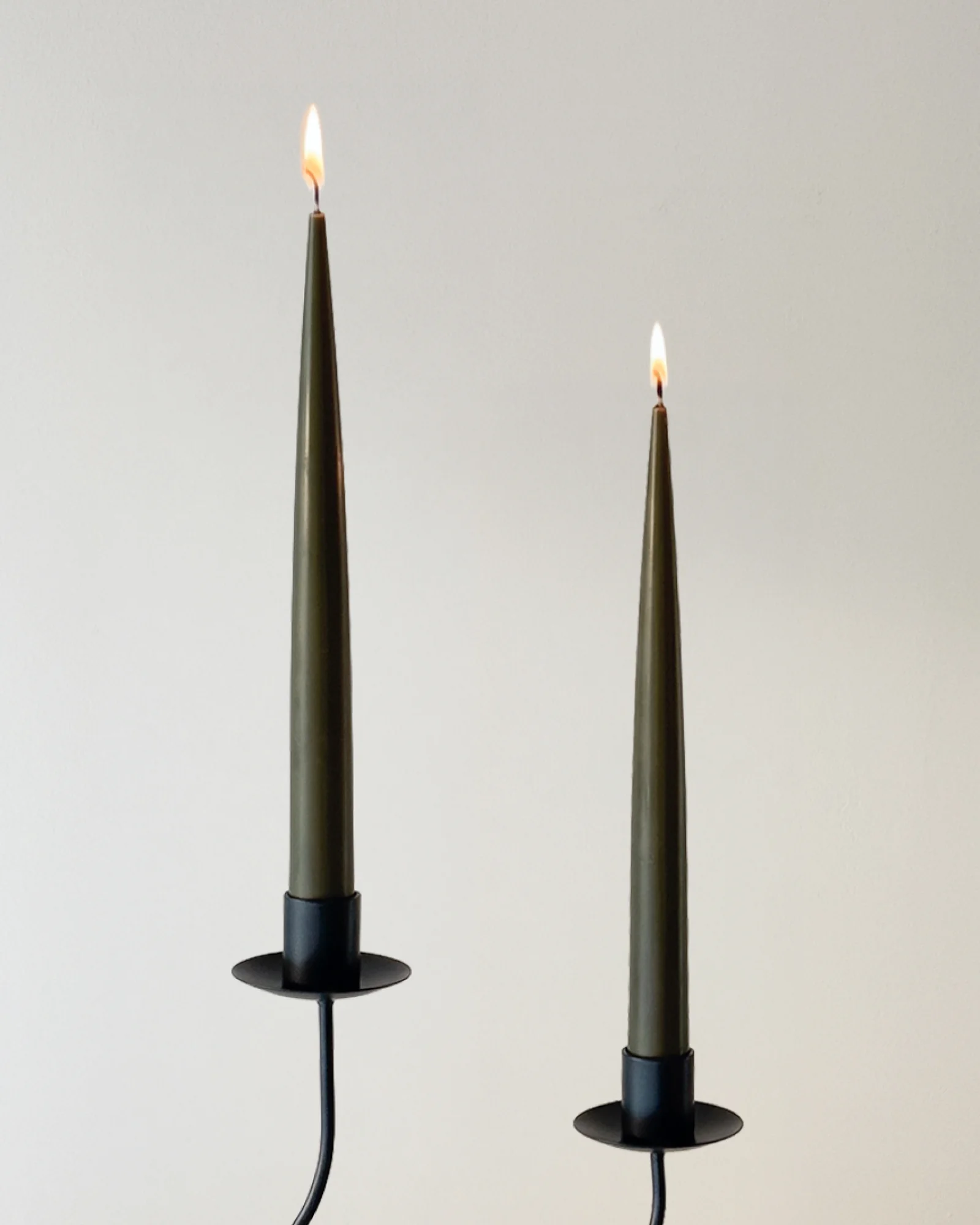 Two lit Deep Pine taper candles displayed in black candle holders Короткая версия: Lit Deep Pine taper candles in black holders