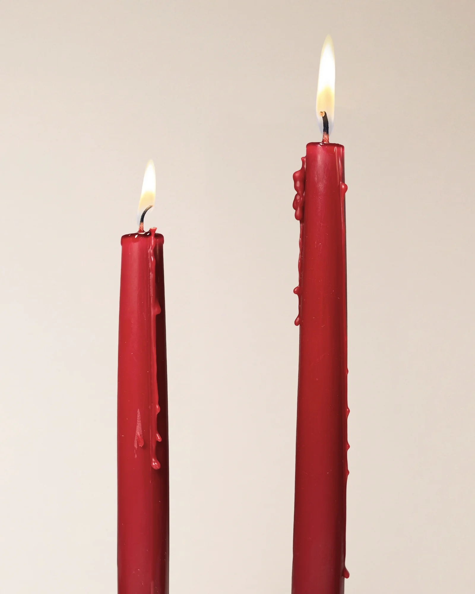 Two lit Vivid Red taper candles with wax dripping down the sides