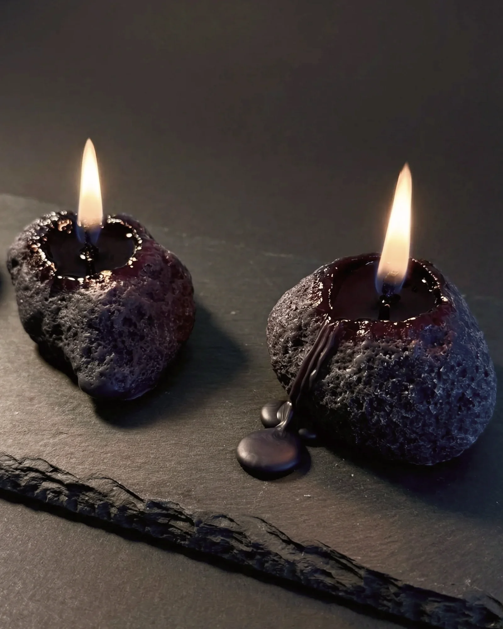 Two Volcanic Stone candles burning on slate, melted wax pooling around the wicks.