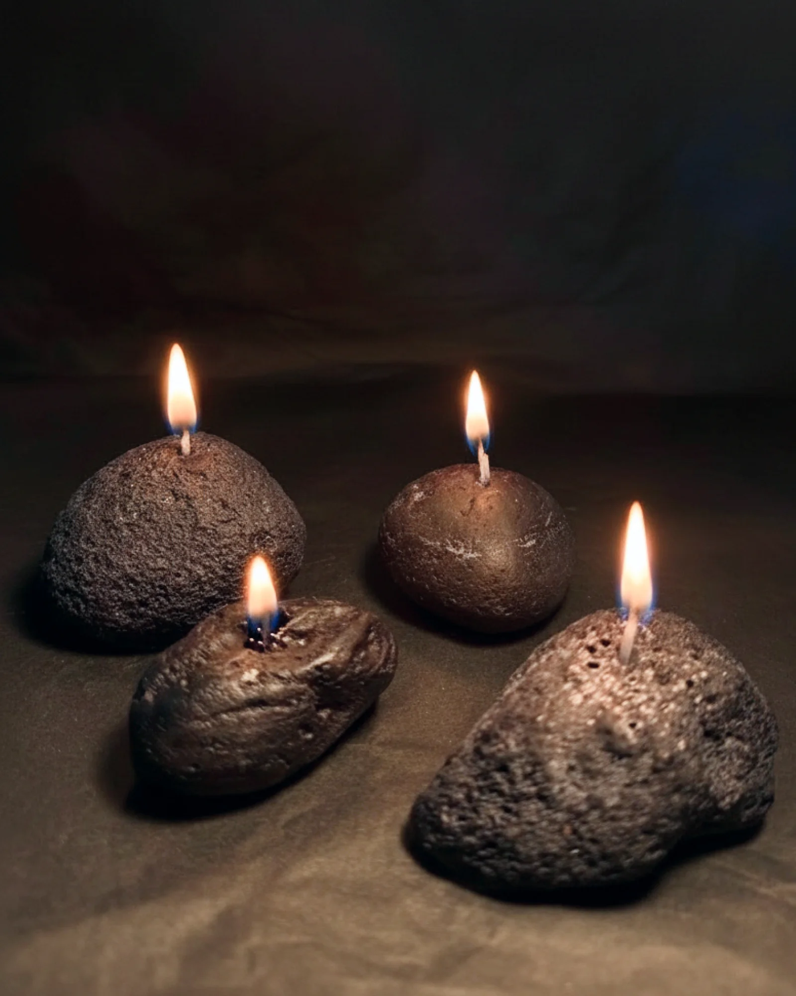 Four lit Volcanic Stone candles glowing in the dark, light catching their porous surfaces.