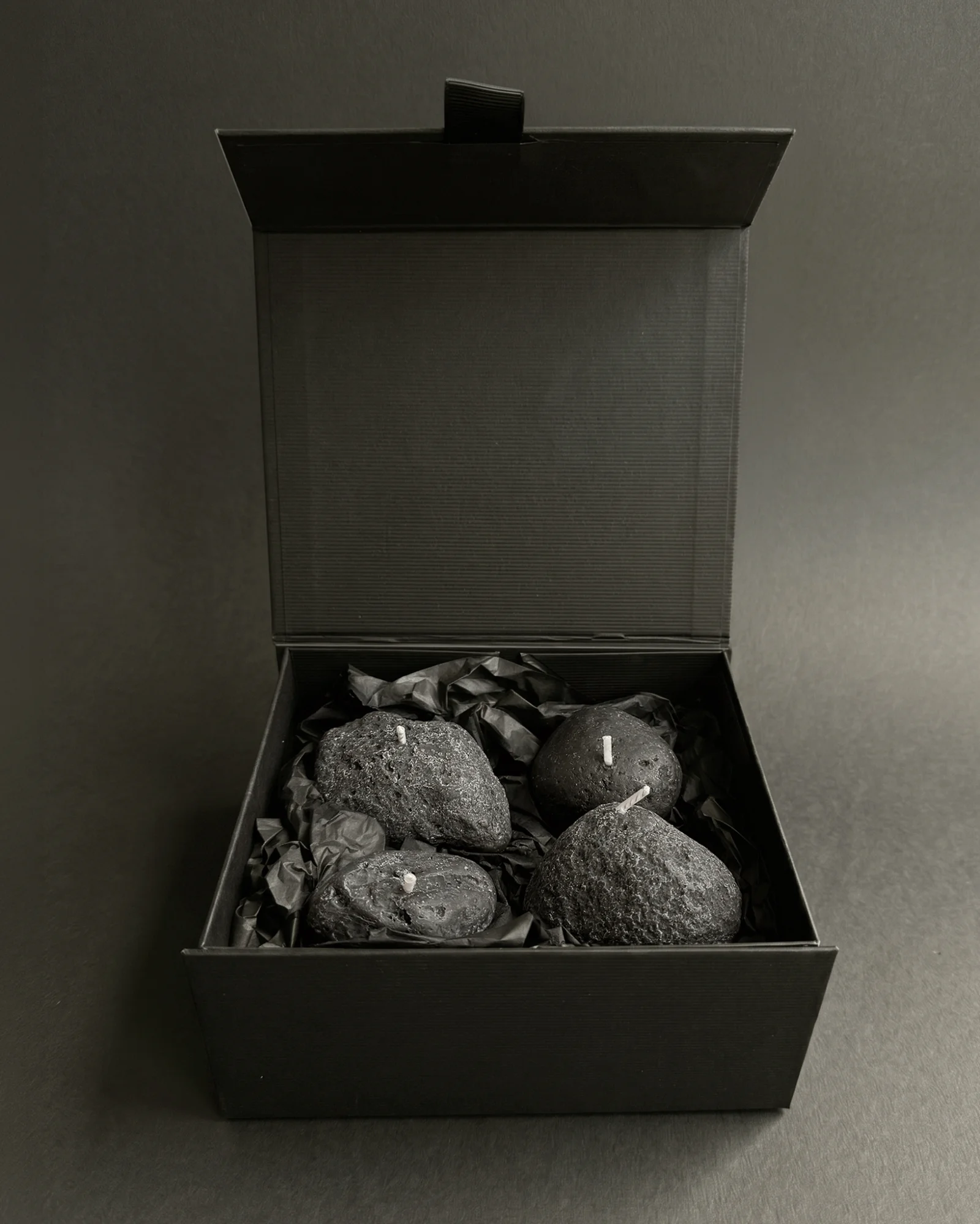 Four Volcanic Stone candles nestled in black tissue inside an open black gift box.