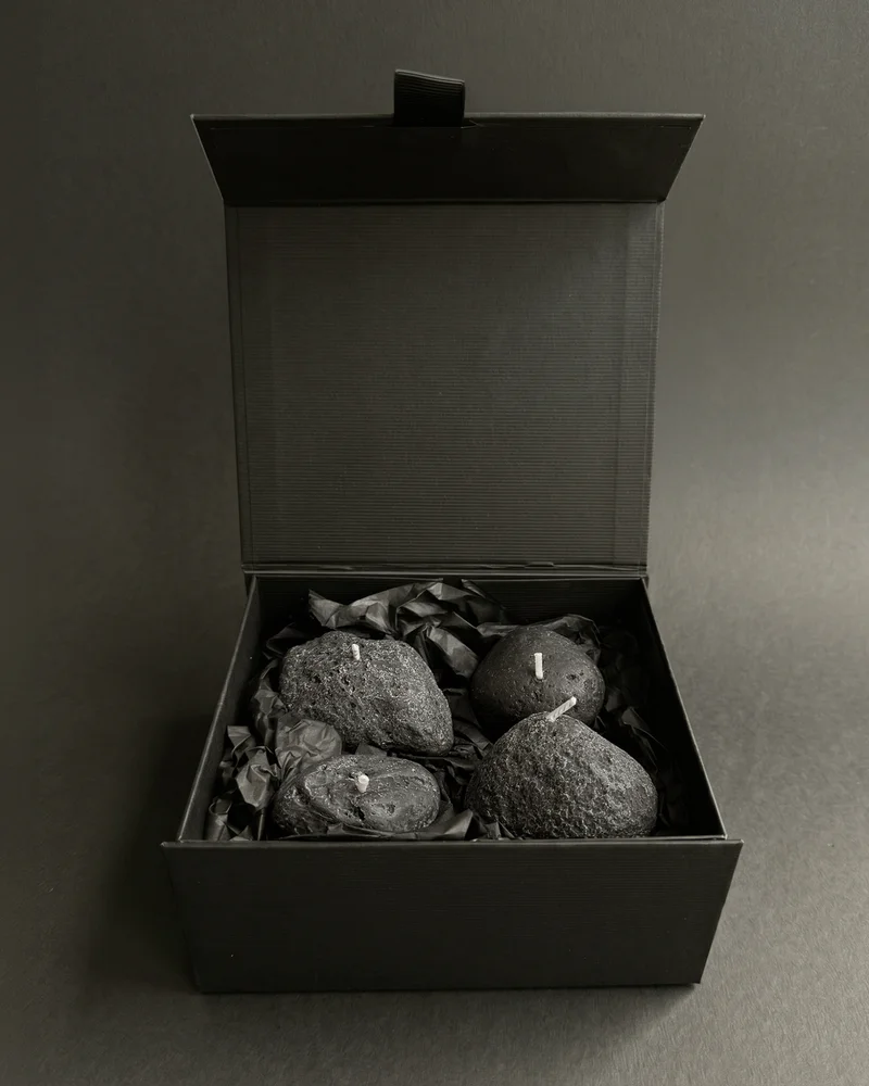 Four Volcanic Stone candles nestled in black tissue inside an open black gift box.